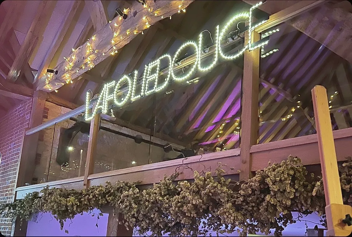 A neon sign and purple lights over the bar at a party in the barn