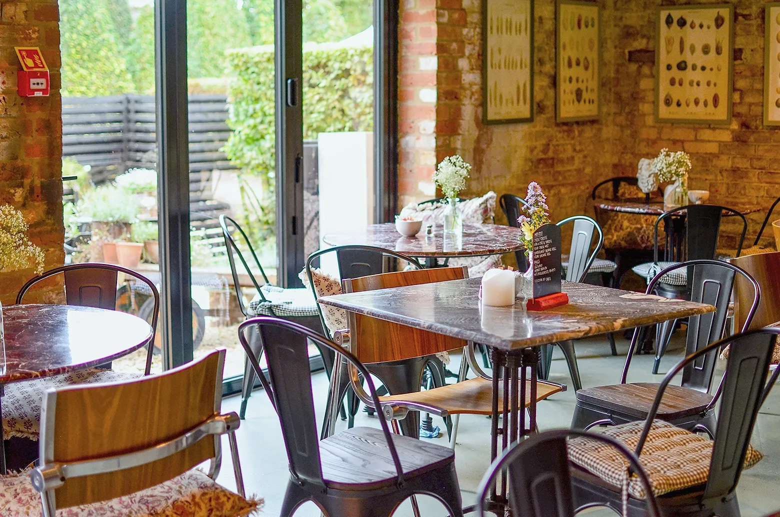 Inside the Hop Kiln Café, marble-topped tables and metal chairs by open glass doors to the terrace