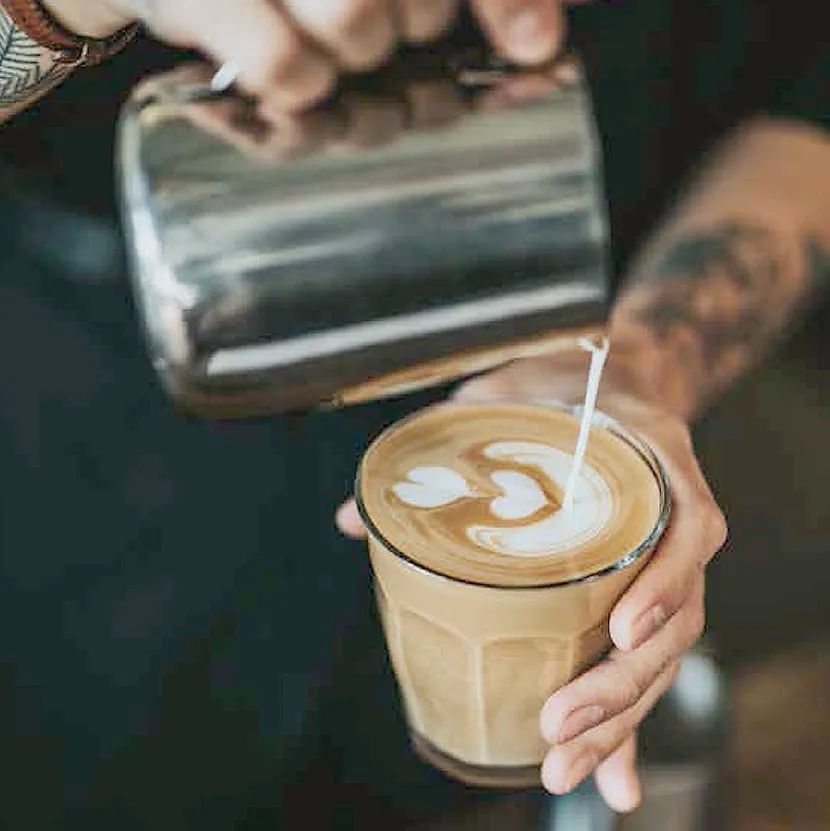 A barista pouring latte art into a glass of coffee at the Hop Kiln Café