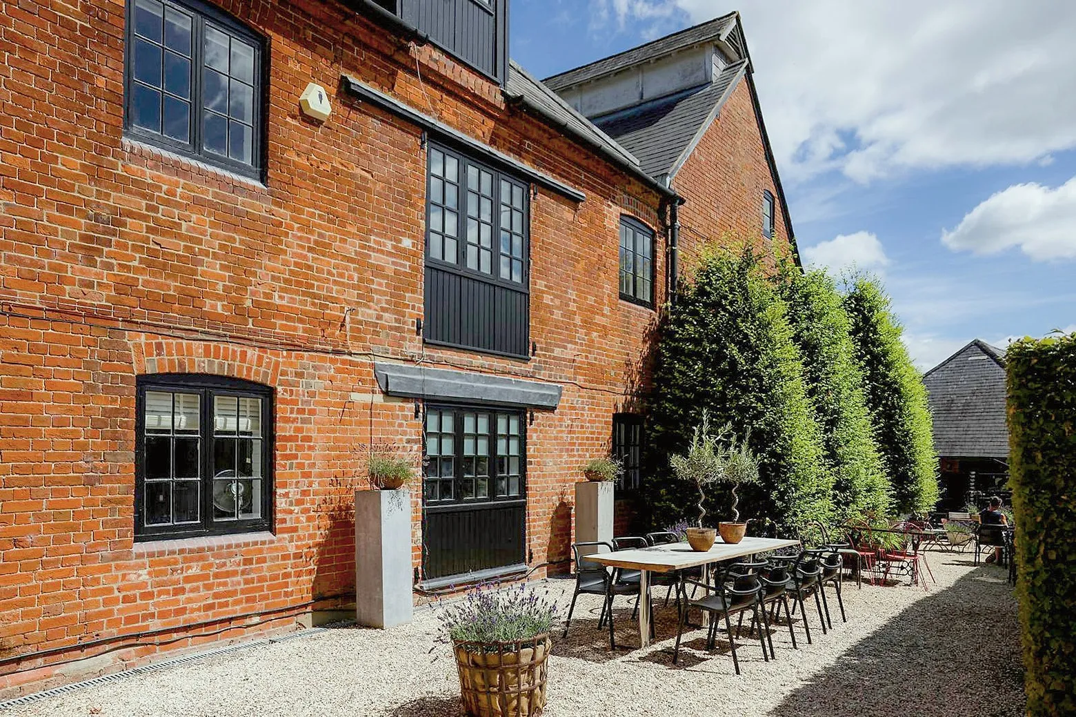 The red-brick Hop Kiln with outdoor tables on the gravel terrace under a blue sky