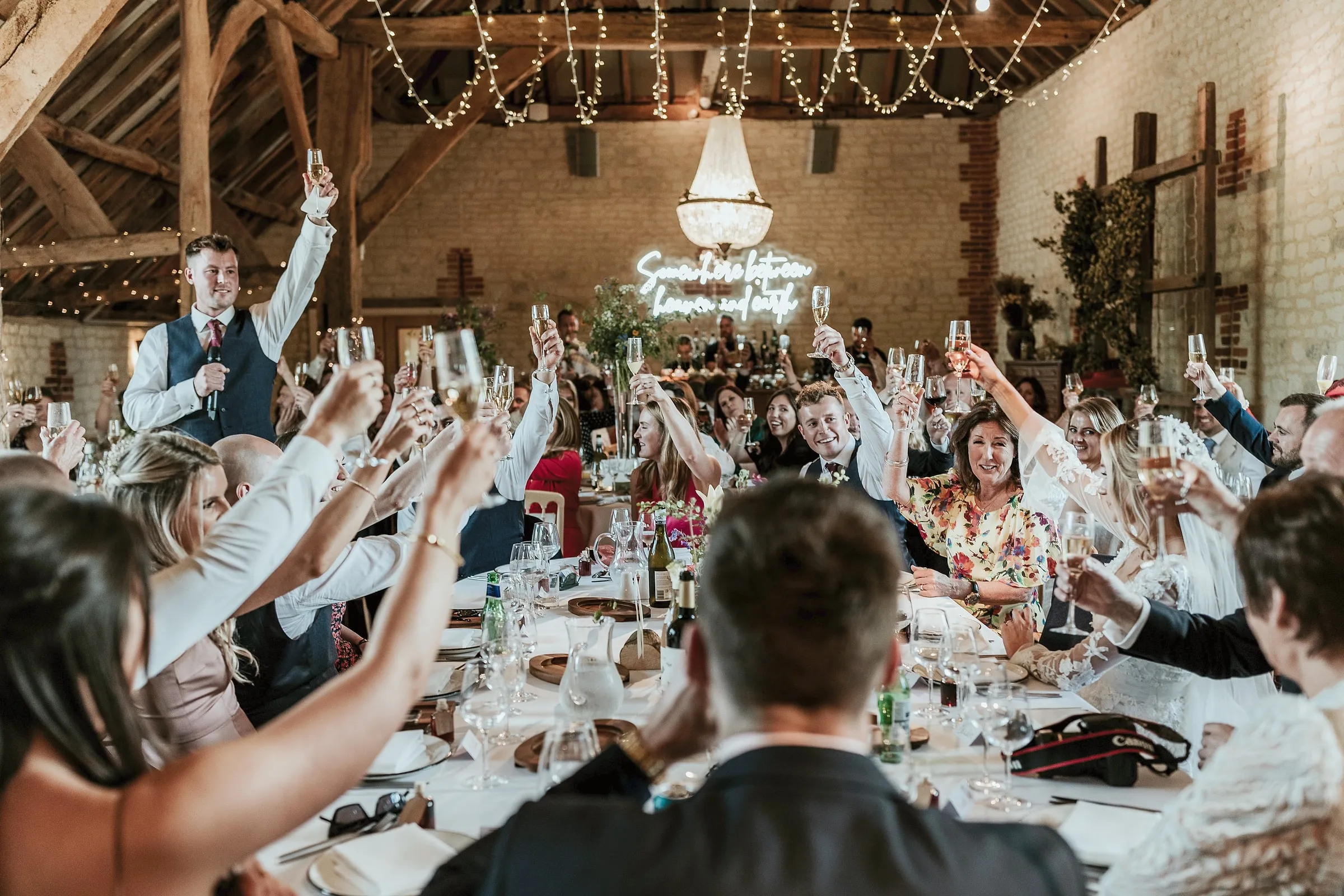 Guests at long tables raising their glasses in the barn under fairy lights