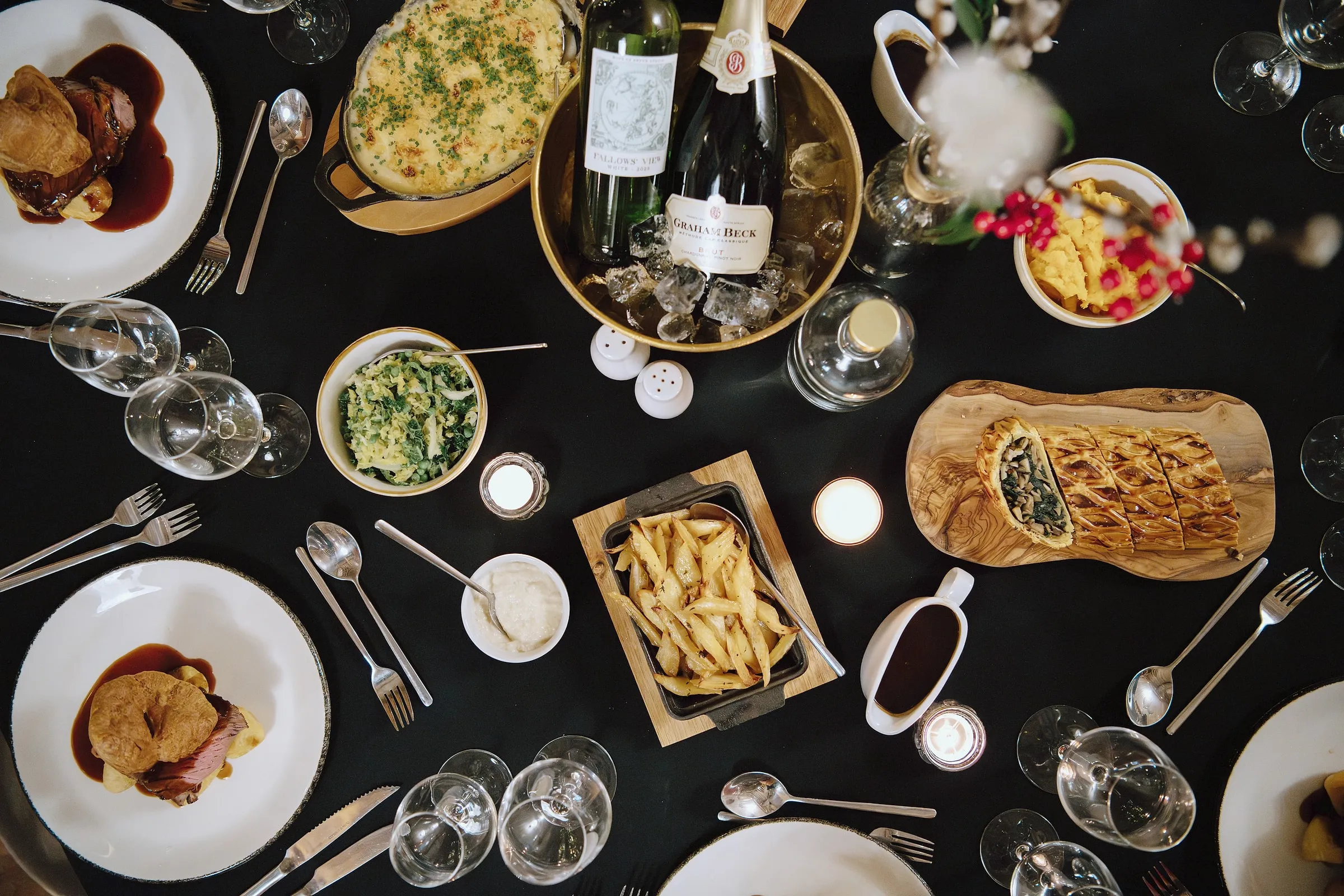 An evening dinner table from above: pies, roast potatoes, greens and wine