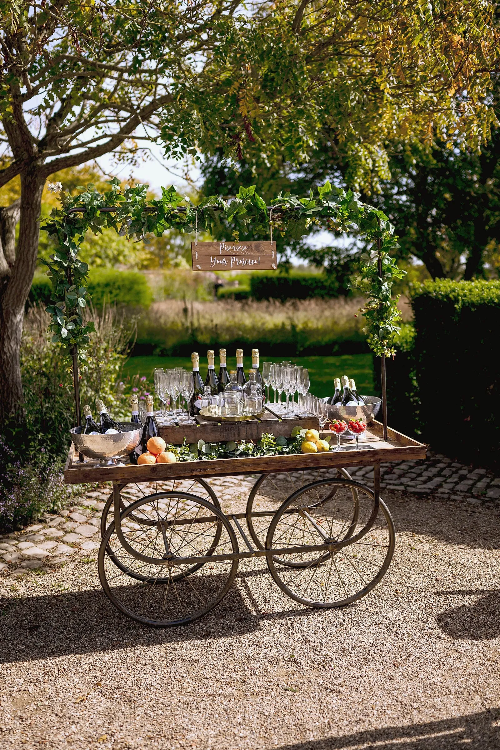 A drinks cart laid with glasses and bottles in the garden, ready for the reception