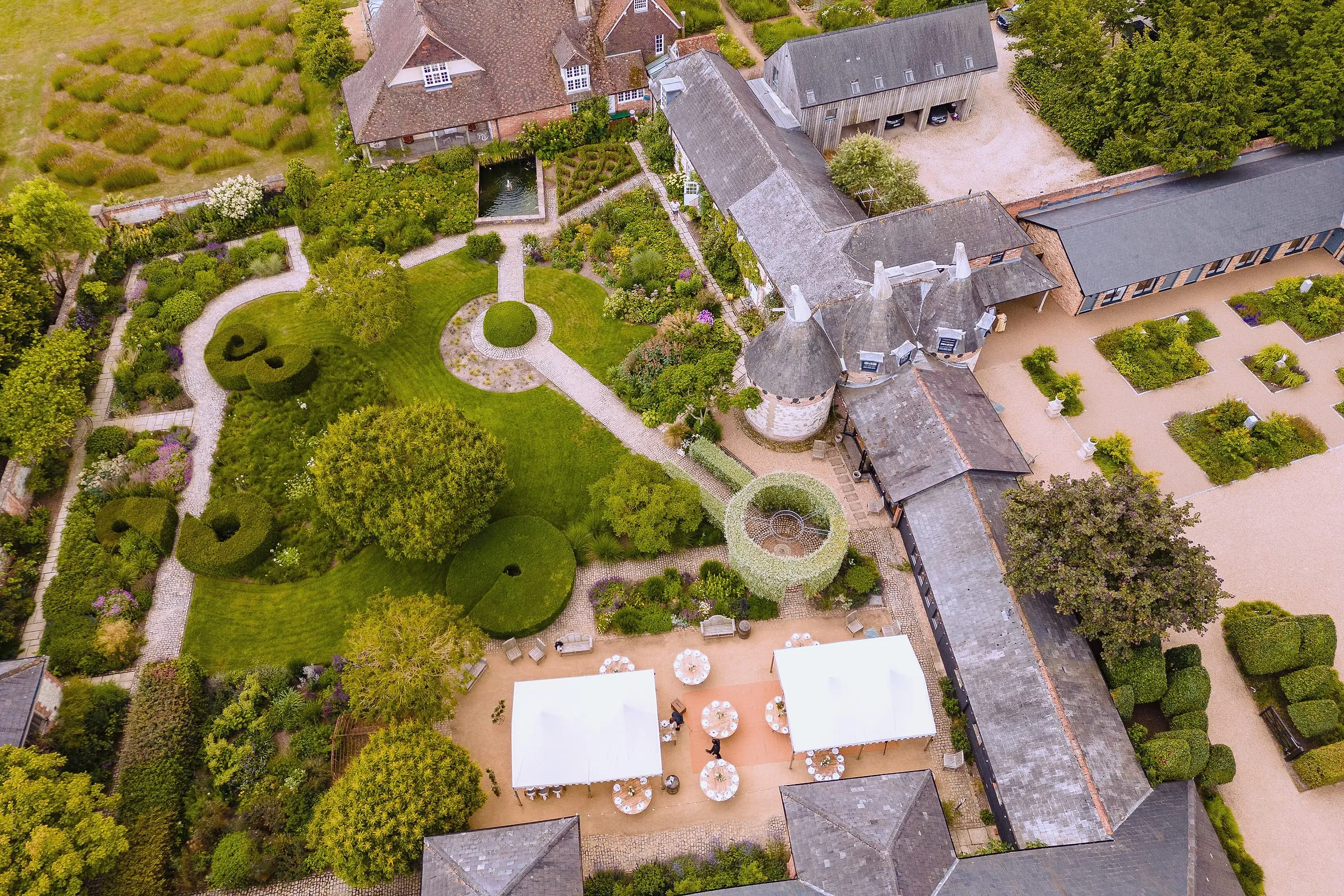 Aerial view of Bury Court's gardens, oast house and courtyard with two white canopies set for a wedding