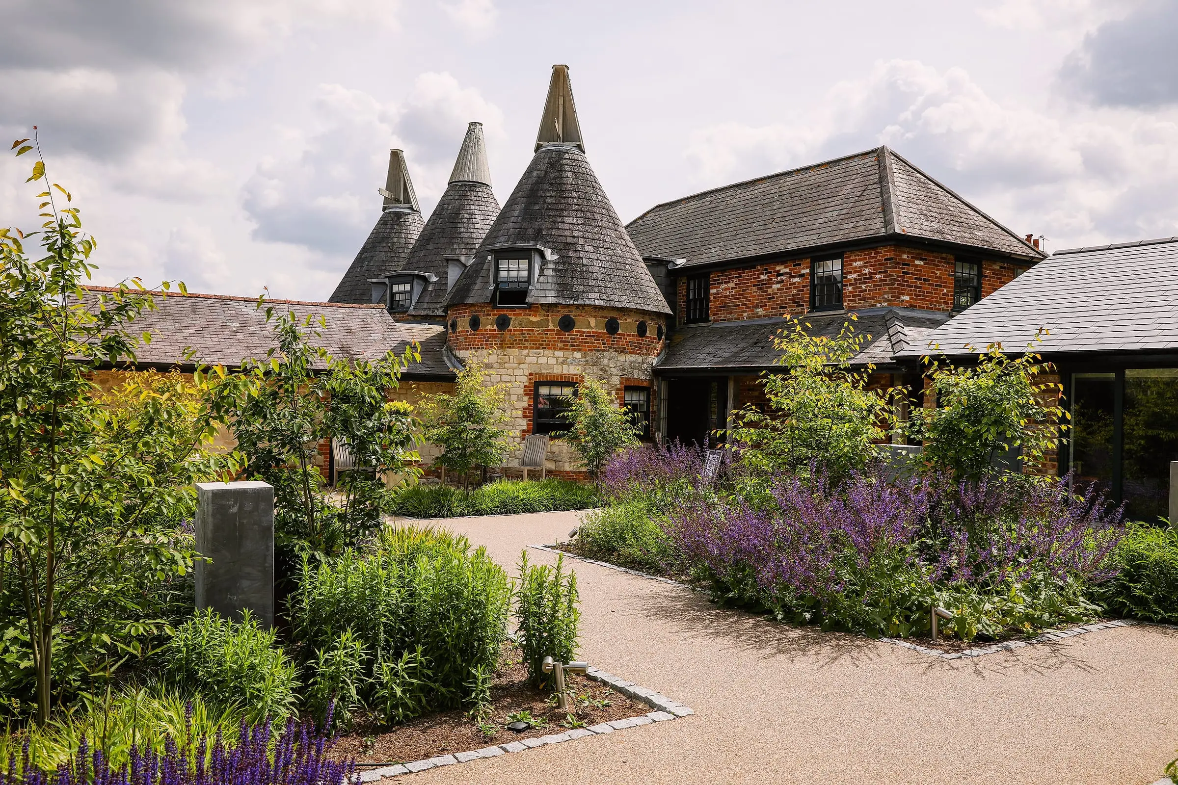 Three oast roundels above the entrance courtyard, with salvia and young trees along the drive