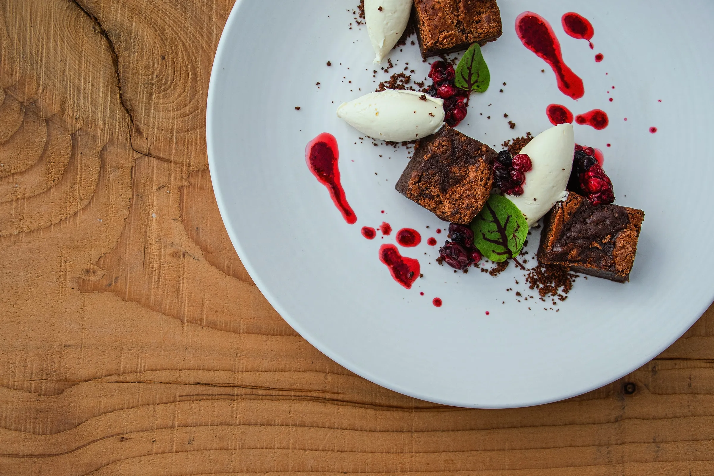 A plated dessert with cream and berry sauce on a wooden table