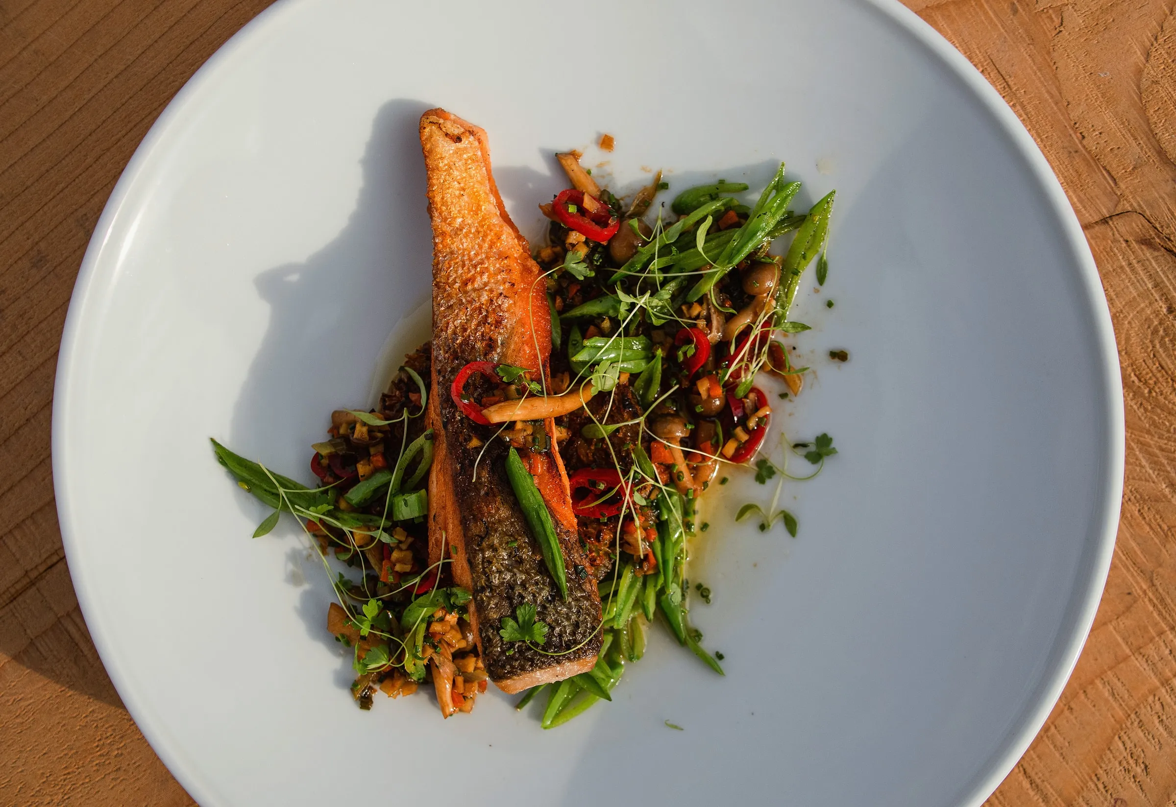Seared salmon on a warm grain salad with green beans and chilli, on a white plate on oak