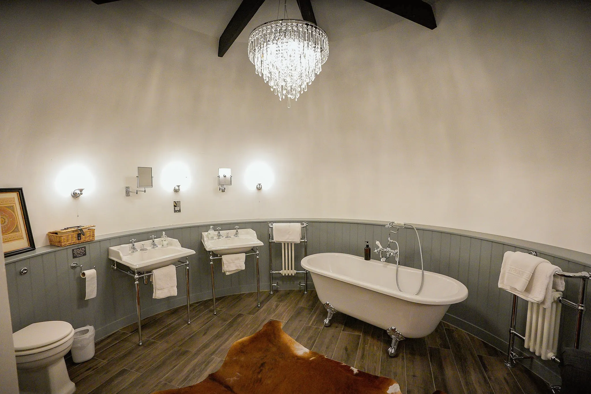 Round bathroom with a roll-top bath, twin basins and a crystal chandelier