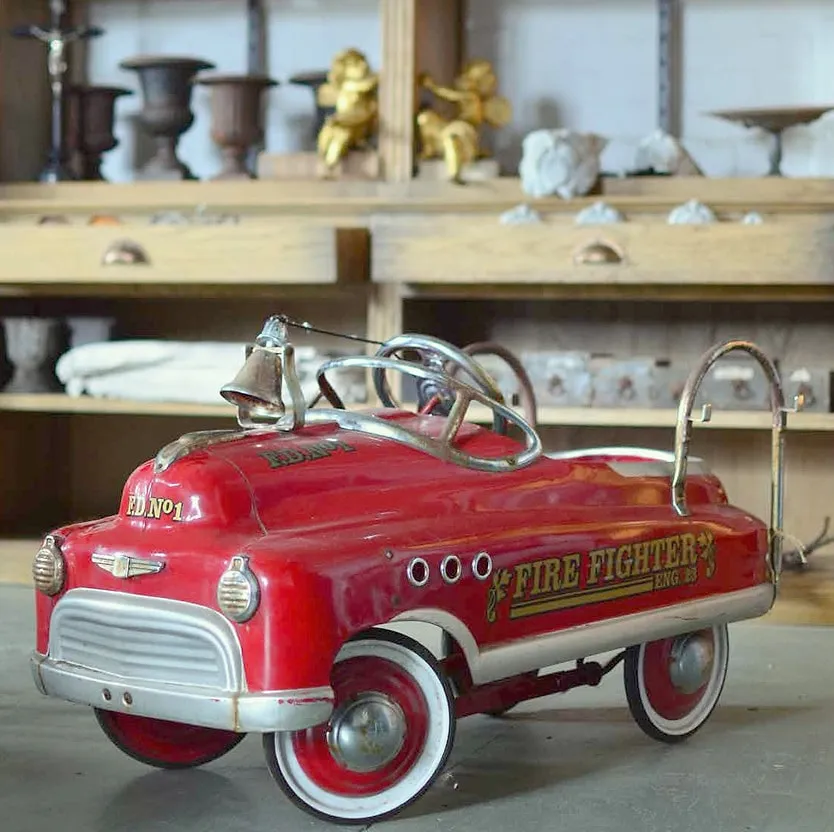 A vintage red toy fire engine among antiques on a shop shelf