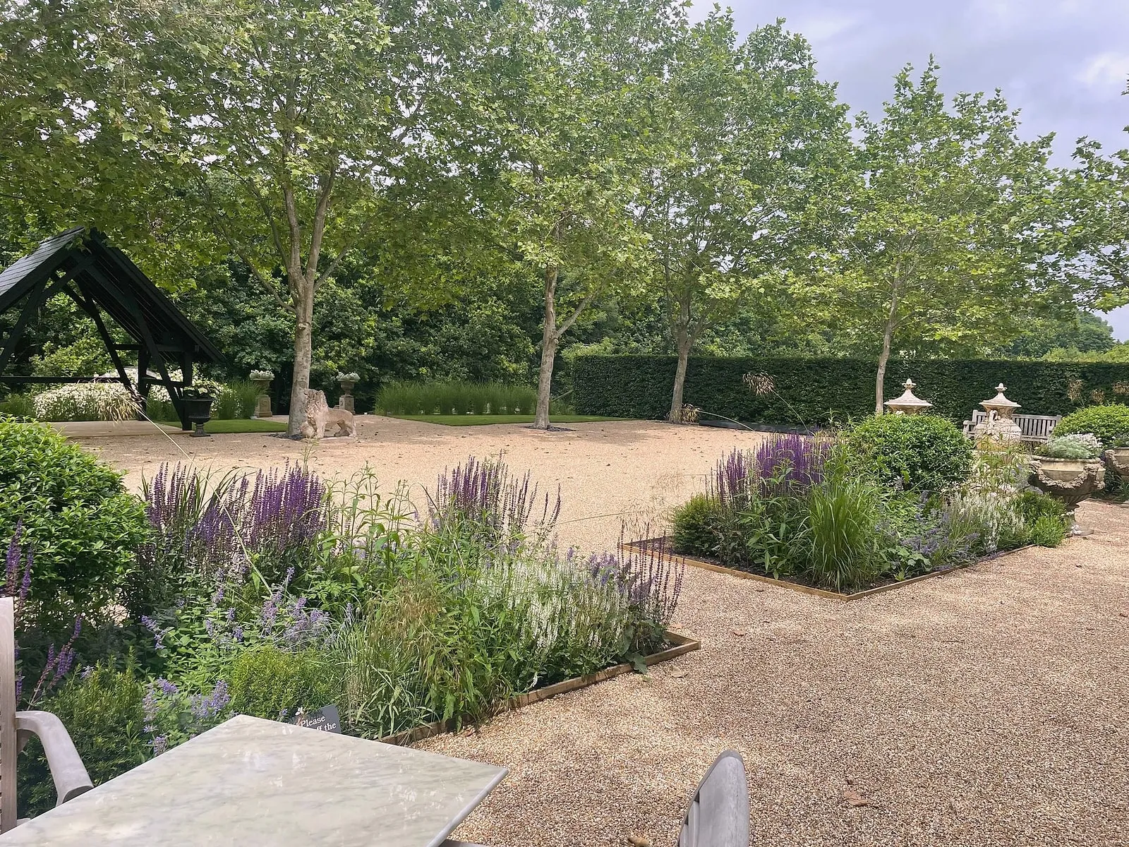 A quiet gravel garden with lavender and salvia beds, a stone table and plane trees