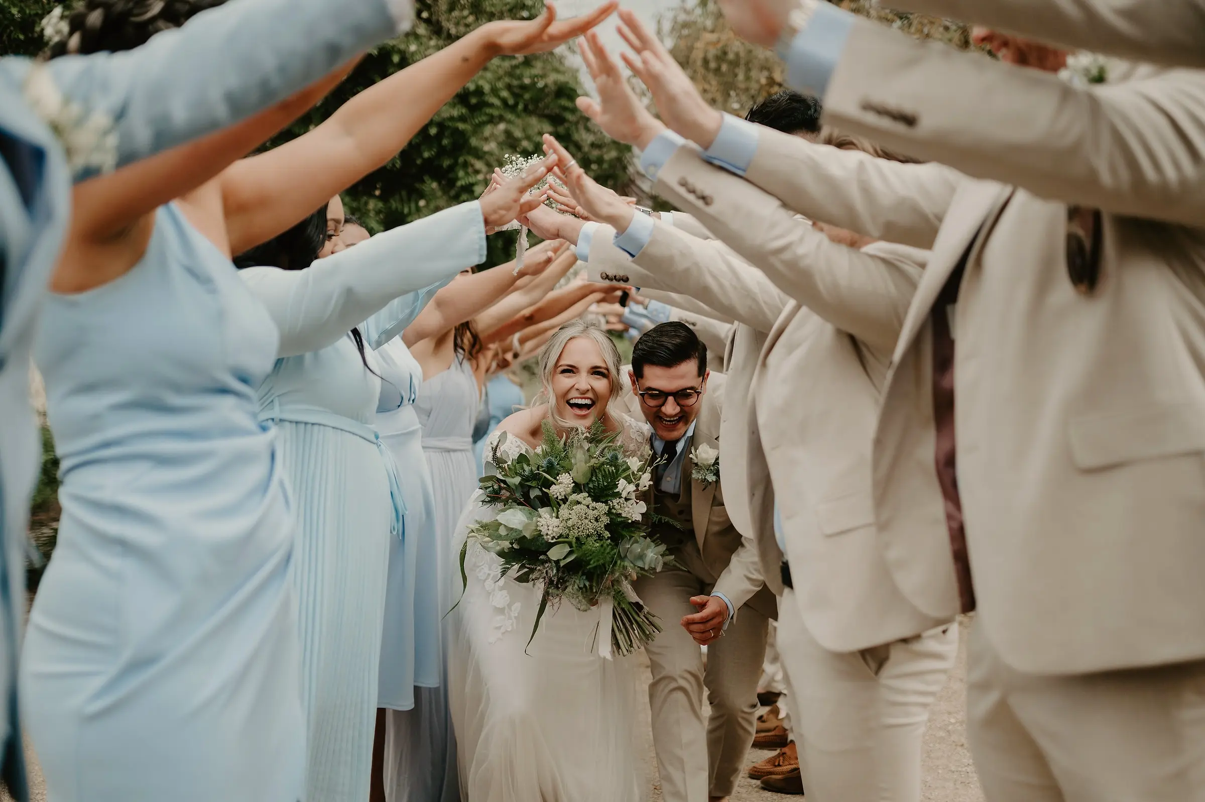 Bride and groom laughing as they run through an arch of raised arms from their wedding party